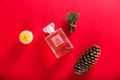 A bottle of perfume among the decor of Christmas tree branches, tangerine and cones on a red background