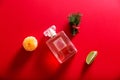 A bottle of perfume among the decor of Christmas tree branches, tangerine and lime on a red background