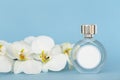 Bottle of perfume with flowers orchids on pastel blue background.