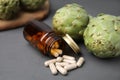 Bottle with pills and fresh artichokes on grey wooden table, closeup Royalty Free Stock Photo