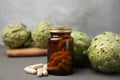 Bottle with pills and fresh artichokes on grey wooden table, closeup Royalty Free Stock Photo