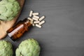 Bottle with pills and fresh artichokes on grey wooden table, flat lay. Space for text Royalty Free Stock Photo