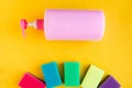 Bottle with pink dishwashing liquid and multicolor sponges on bright yellow background. Royalty Free Stock Photo