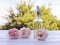 Bottle with a pipette and rose oil lies on a wooden table in a Sunny garden next to delicate pink fragrant flowers Royalty Free Stock Photo