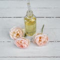 Bottle with a pipette and rose oil lies on a wooden table in the garden next to the delicate pink fragrant flowers Royalty Free Stock Photo