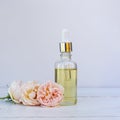 Bottle with a pipette and rose oil lies on a wooden table in the garden next to the delicate pink fragrant flowers Royalty Free Stock Photo