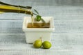 Bottle pouring virgin olive oil in white breakfast square bowl with raw green turkish olives on white rustic vintage wooden table. Royalty Free Stock Photo