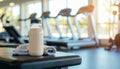 Bottle of protein shake and towel on bench in gym with treadmills Royalty Free Stock Photo