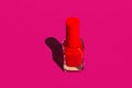 Bottle with red crimson nail polish on solid fuchsia pink violet background in bright sunlight strong shadows