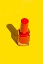 Bottle with red crimson nail polish on solid yellow background. Bright sunlight strong shadows. Creative minimalist funky style