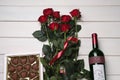 Bottle of red wine, beautiful roses and heart shaped chocolate candies on white wooden table, flat lay Royalty Free Stock Photo