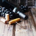 Bottle of red wine with fresh grape and bunch of corks on wooden table Royalty Free Stock Photo