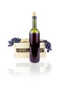 Bottle of red wine in front of wooden box with bunches of grapes and paper shavings. Isolated on white background Royalty Free Stock Photo