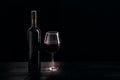 Bottle of red wine and a glass half filled with red wine, on a wooden black table, black background Royalty Free Stock Photo