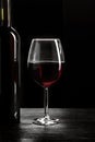 Bottle of red wine and a glass half filled with red wine, on a wooden black table, black background Royalty Free Stock Photo