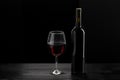 Bottle of red wine and a glass half filled with red wine, on a wooden black table, black background Royalty Free Stock Photo