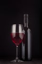 Bottle of red wine and wine glass mock up on elegant dark black wooden background, vertical. Royalty Free Stock Photo