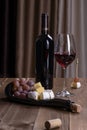 A bottle of red wine, a glass with red wine, a board with snacks