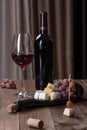 A bottle of red wine, a glass with red wine, a board with snacks