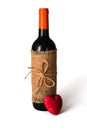 Bottle of red wine wrapped in burlap tied with twine and red heart on white background. Valentine`s Day. Close-up Royalty Free Stock Photo