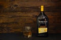 A bottle of Ron Barcelo, Anejo Dominican rum and a glass with ice on a dark wooden background. Ron Barcelo is a blend of