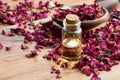 A bottle of rose essential oil with dried rose petals on a wooden table Royalty Free Stock Photo