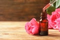 Bottle of rose essential oil, pipette and flowers on wooden table Royalty Free Stock Photo