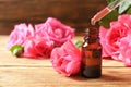 Bottle of rose essential oil, pipette and flowers on wooden table Royalty Free Stock Photo