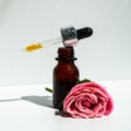 A bottle of rose oil with fresh flowers on a white background. Rose oil.