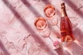 Bottle of rose sparkling wine, two filled wine glasses and rosebud on textured pink background with daylight and strong Royalty Free Stock Photo