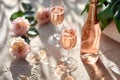 Bottle of rose sparkling wine, two filled wine glasses and rosebuds on textured pink background with daylight and strong Royalty Free Stock Photo