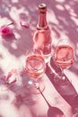 Bottle of rose sparkling wine, two filled wine glasses and rosebuds on textured pink background with daylight and strong Royalty Free Stock Photo