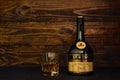 A bottle of Saint-Remy Authentic VSOP French brandy and a glass with ice on a dark wooden background. A brandy with an