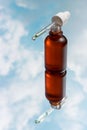 Bottle with serum and pipette close-up against background of sky and clouds.