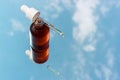 Bottle with serum and pipette close-up against background of sky and clouds.