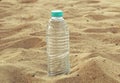 Bottle with sparkling crystal drinking water with a red lid on the sand on a background of the beach on a hot sunny
