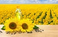 Bottle of sunflower oil with flowers and seed of sunflower on wooden table on background blossoming field of sunflowers