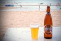 Bottle of Thai beer with a full plastic glass on a beach with people in Thailand. The beach and people are blur, there is a vignet Royalty Free Stock Photo