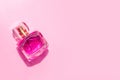 Bottle of transparent female perfume on pink background.