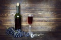 Bottle and transparent wineglass with red wine and bunch of grapes on brown wooden plank surface, corkscrew nearby Royalty Free Stock Photo