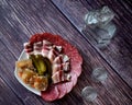 A bottle and two glasses of vodka are on a wooden table, next to a plate with an assortment of meat snacks
