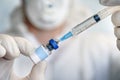 bottle of vaccine close-up in the hand of a doctor with white gloves on a blue background