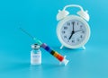 Bottle of vaccine, syringe and alarm clock on a blue background. Vaccination against the flu, infections, covid Royalty Free Stock Photo