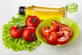 Vegetable oil, salad from tomato in bowl, salt shaker, tomatoes on leaves of lettuce on wooden table