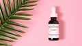 Bottle of a vitamin C serum resting on a pastel pink background next to a tropical green leaf