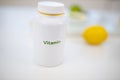 Bottle of vitamins on white table with limes and lemons as background