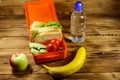 Bottle of water, apple, banana and lunch box with sandwiches and fresh vegetables on wooden table