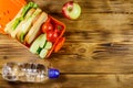 Bottle of water, apple and lunch box with sandwiches and fresh vegetables on a wooden table