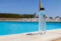 a bottle of water in his hand against a pool background as a symbol of a lack of water in the body in the summer