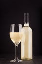 Bottle of white wine and wine glass mock up on elegant dark black wooden background, vertical. Royalty Free Stock Photo